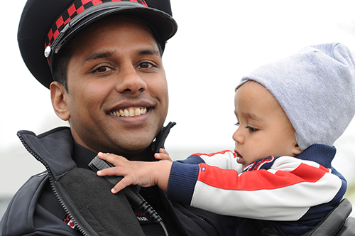 A male Auxiliary officer holds a toddler in his arms